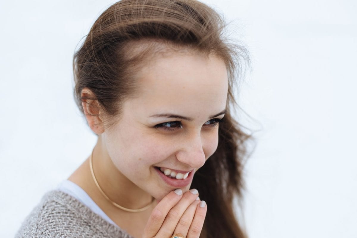 A young girl smiling with her hands near her mouth