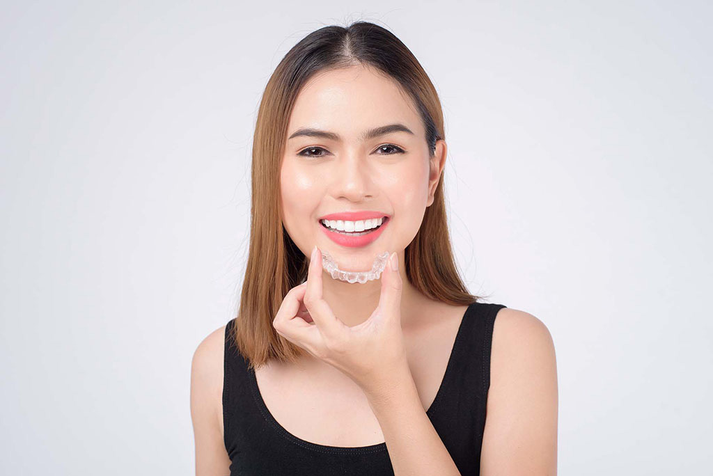 Invisalign at Gulf Coast Orthodontics young woman smiling with beautiful straight white teeth and holding Invisalign aligners